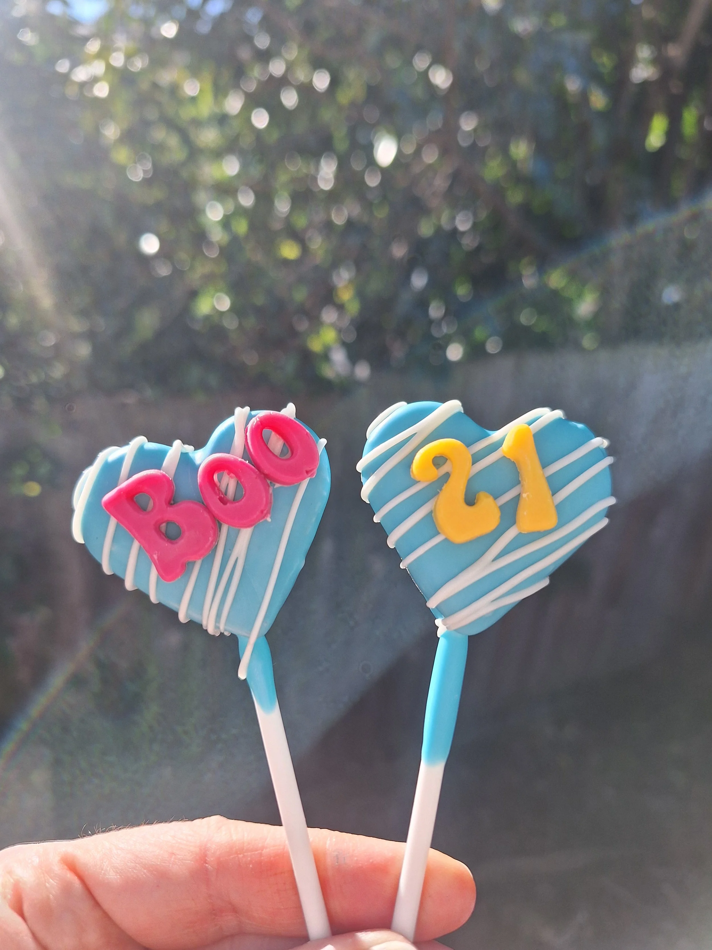 Two blue heart-shaped cake pops with white drizzle and colourful birthday numbers
